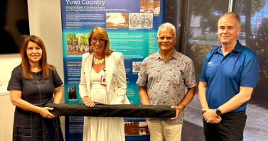 Northern Queensland PHN CEO Sean Rooney (right), Executive Director Health Service Integration and Innovation Karin Barron (left), and Traditional Custodian Elder for the Mackay region Philip Kemp present Mackay HHS CEO Susan Gannon with an updated 2024 Yuwi banner. 